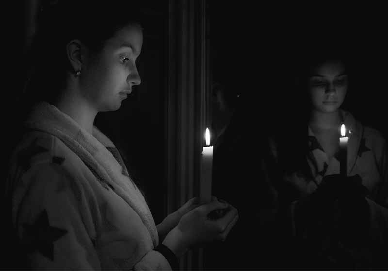 Black and white girl in a dark room with a candle in her hand in front of the mirror 