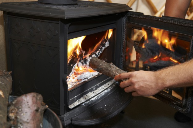The Benefits of Using A Wood Burning Stove On Your Homestead man putting log in fire