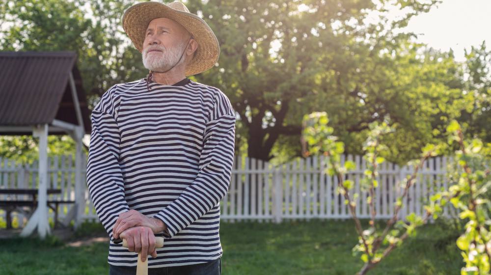 retired man wearing straw hat holding shovel standing in his garden | Ways To Get The Homestead Ready For Spring | ready for spring | preparing a garden bed