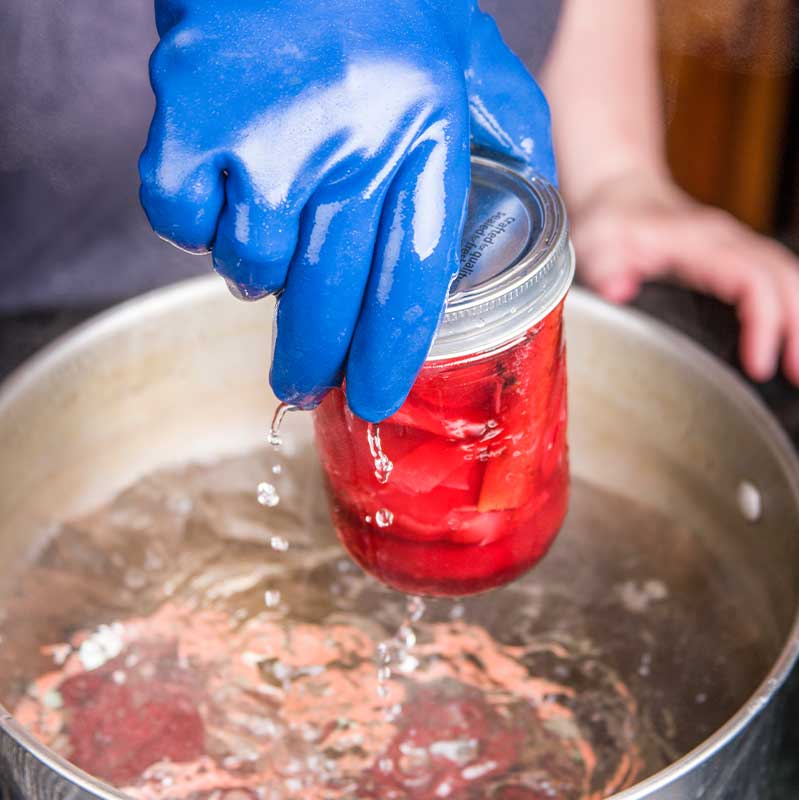 Woman wearing rubber gloves removing canning jars of pickled beets | canning technique