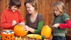 woman helping kids carve their pumpkins | Best Pinterest Halloween Crafts For You And Your Kids | featured