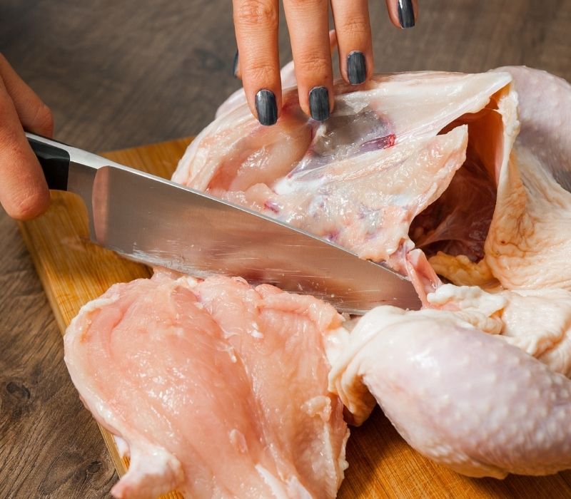 Woman cuts carcass | bone-in chicken breast
