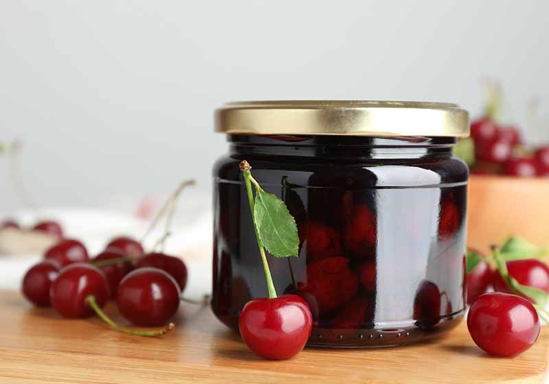Jar of pickled cherries and fresh fruits on wooden board, closeup | canned cherries