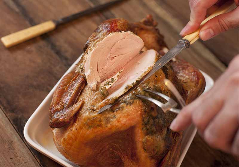 Overhead view of the hands of a man carving a roast turkey with a carving knife and fork slicing the breast meat | cooking turkey breast