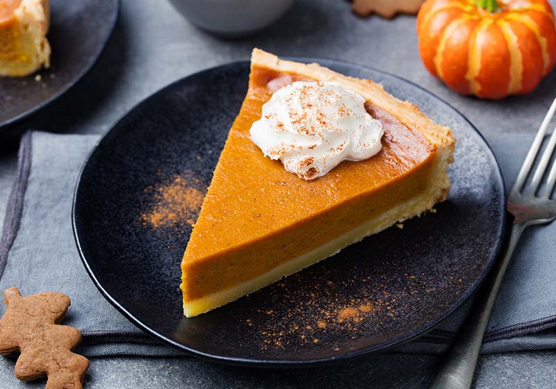 Pumpkin pie, tart made for Thanksgiving day with whipped cream on a black plate | thanksgiving desserts