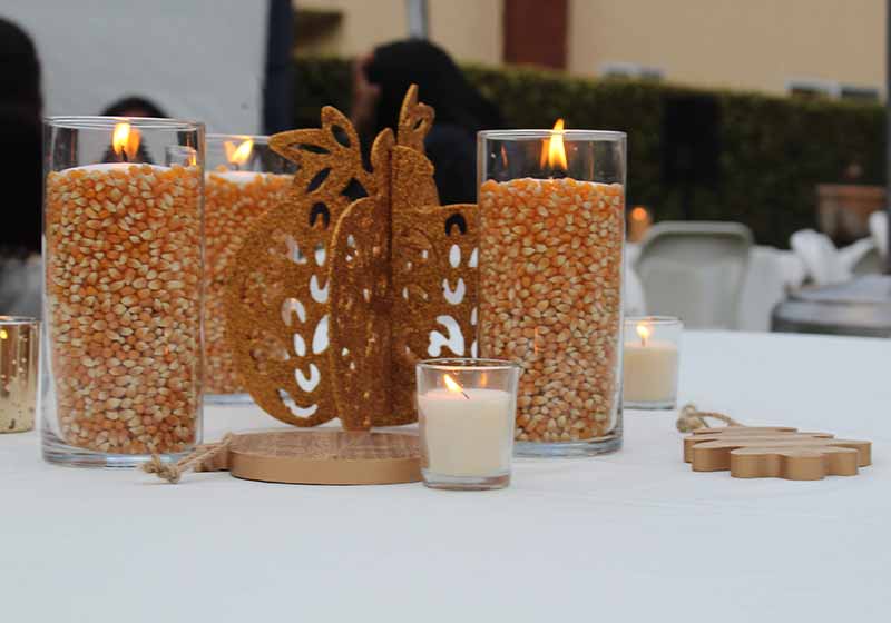 Thanksgiving table centerpiece candles with corn kernels and small white candles on white tablecloth with gold sparkling pumpkin decoration | fall centerpiece