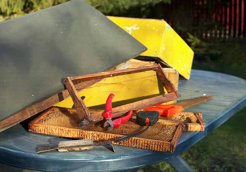 Various hand tools and parts of a bee hive laid on the table outdoor | beekeeping