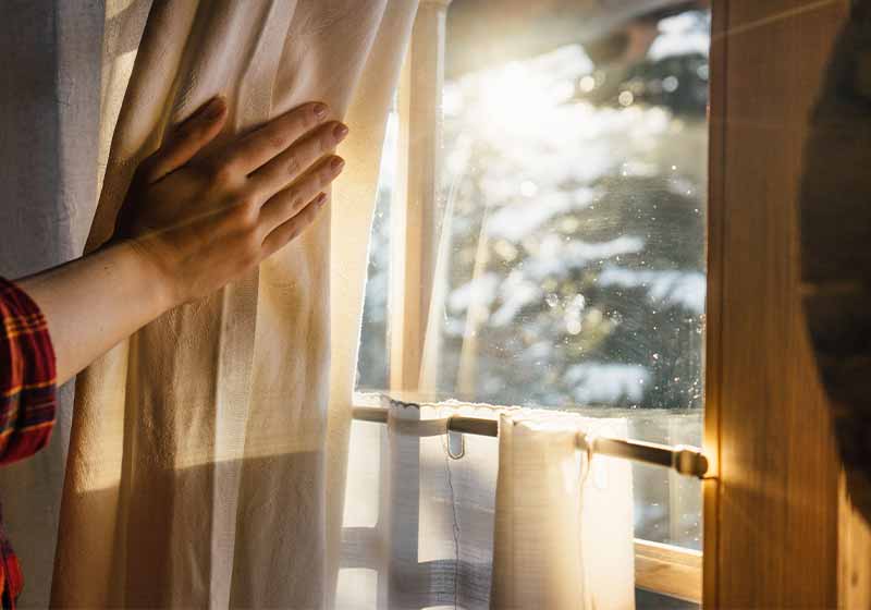 Hand Opens Curtain on the Wooden Cottage House Window | how to stay warm in winter