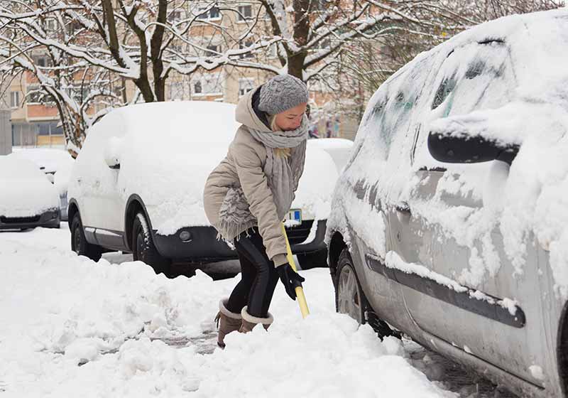Independent woman shoveling her parking lot after a winter snowstorm | snow hacks