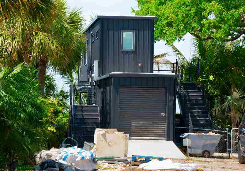 Metal shipping container house under construction with building material products in front yard | Container Studio With A Garage