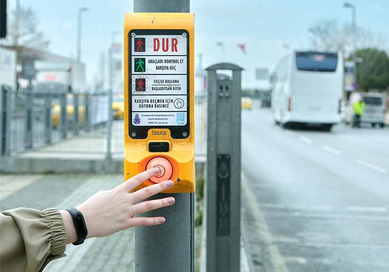 A female hand presses on the transition push button for pedestrians | winter walking tips