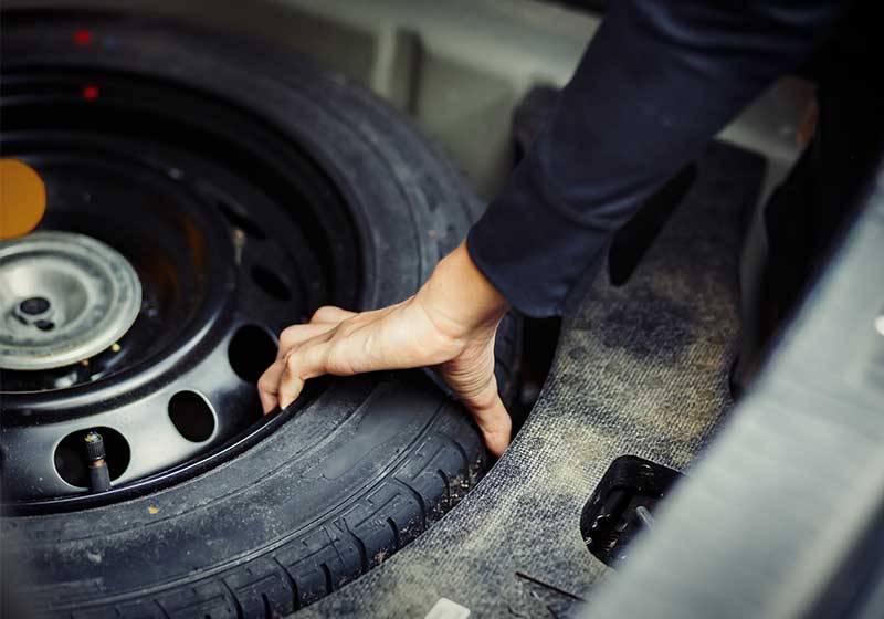 Close up mechanic hand taking spare tire at boot | car survival kit