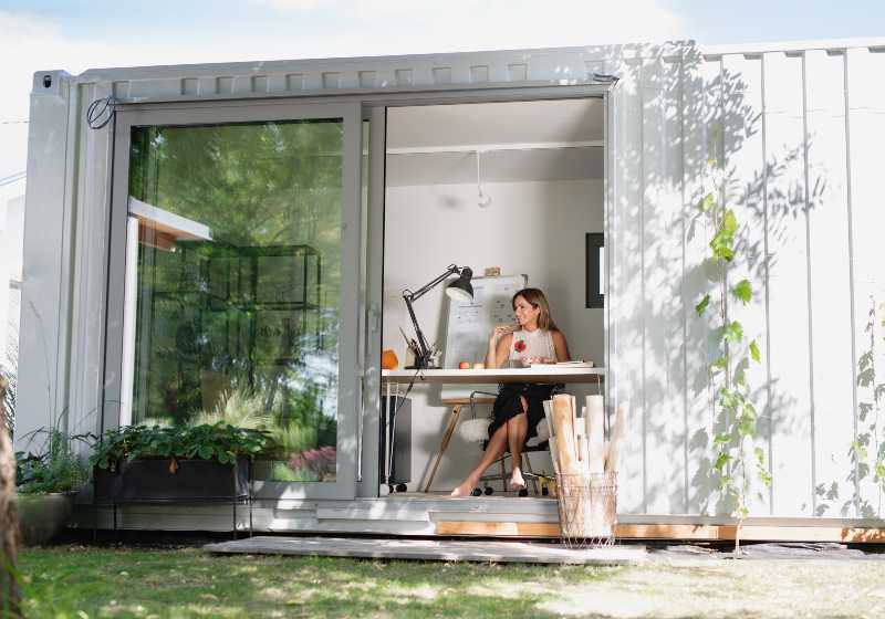 Mature woman working indoors in home office in container house in backyard | Container Home And Studio
