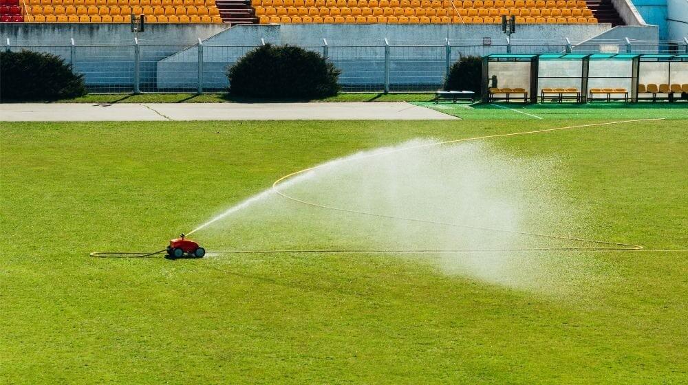 Red mobile sprinkler watering | Tractor Sprinkler FAQs: How Does It Work? | Featured