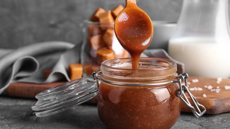 Spoon with tasty caramel sauce over jar on table | Easy Caramel Recipe For A Fall-Tastic Season | featured