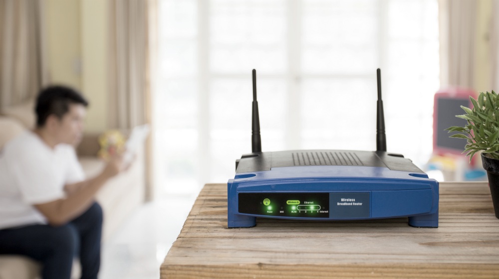 Closeup of a wireless router and a young man using Tablet on living room | How to Speed Up WiFi On A Budget | how to increase internet speed