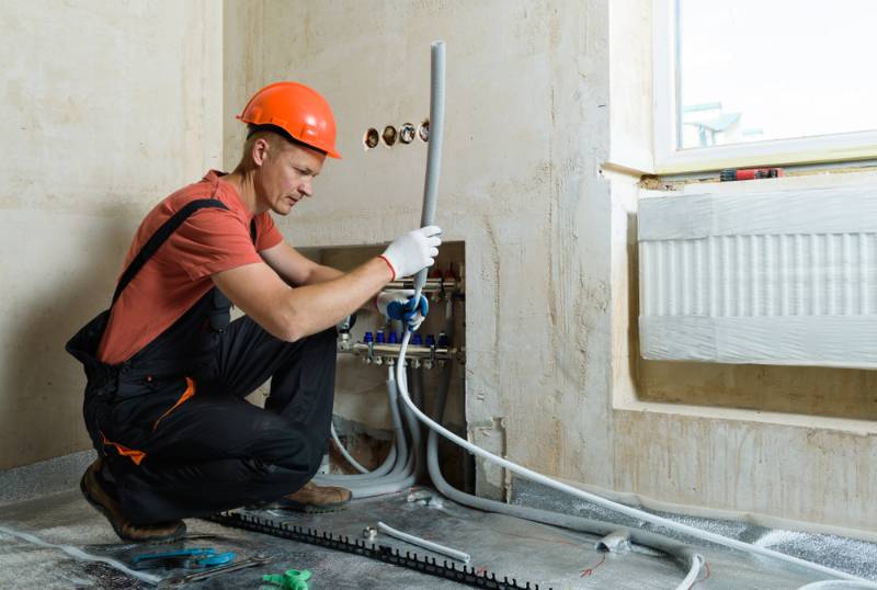 worker-installing-pipe-warm-floor-apartment | Fall Home Maintenance Checklist: How To Prepare Your Home For Fall