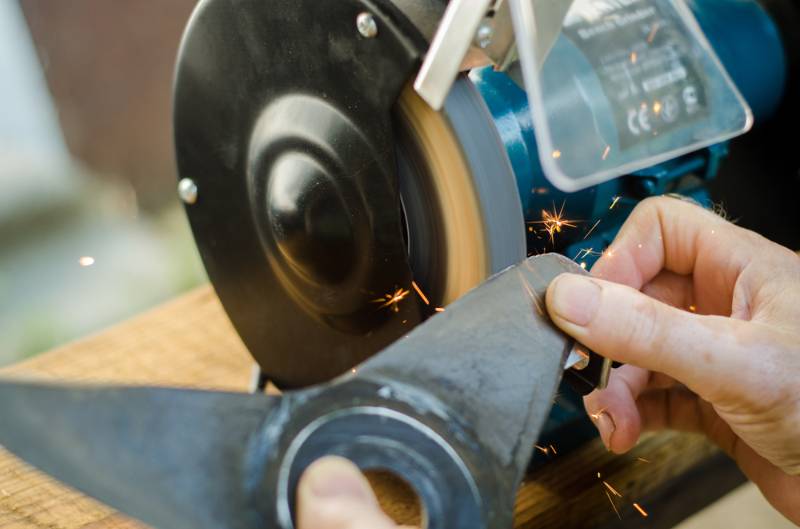 worker sharpening his blade lawn mower | Lawn Mower Repair: Common Problems And How To Fix Them | how to fix a smoking lawn mower