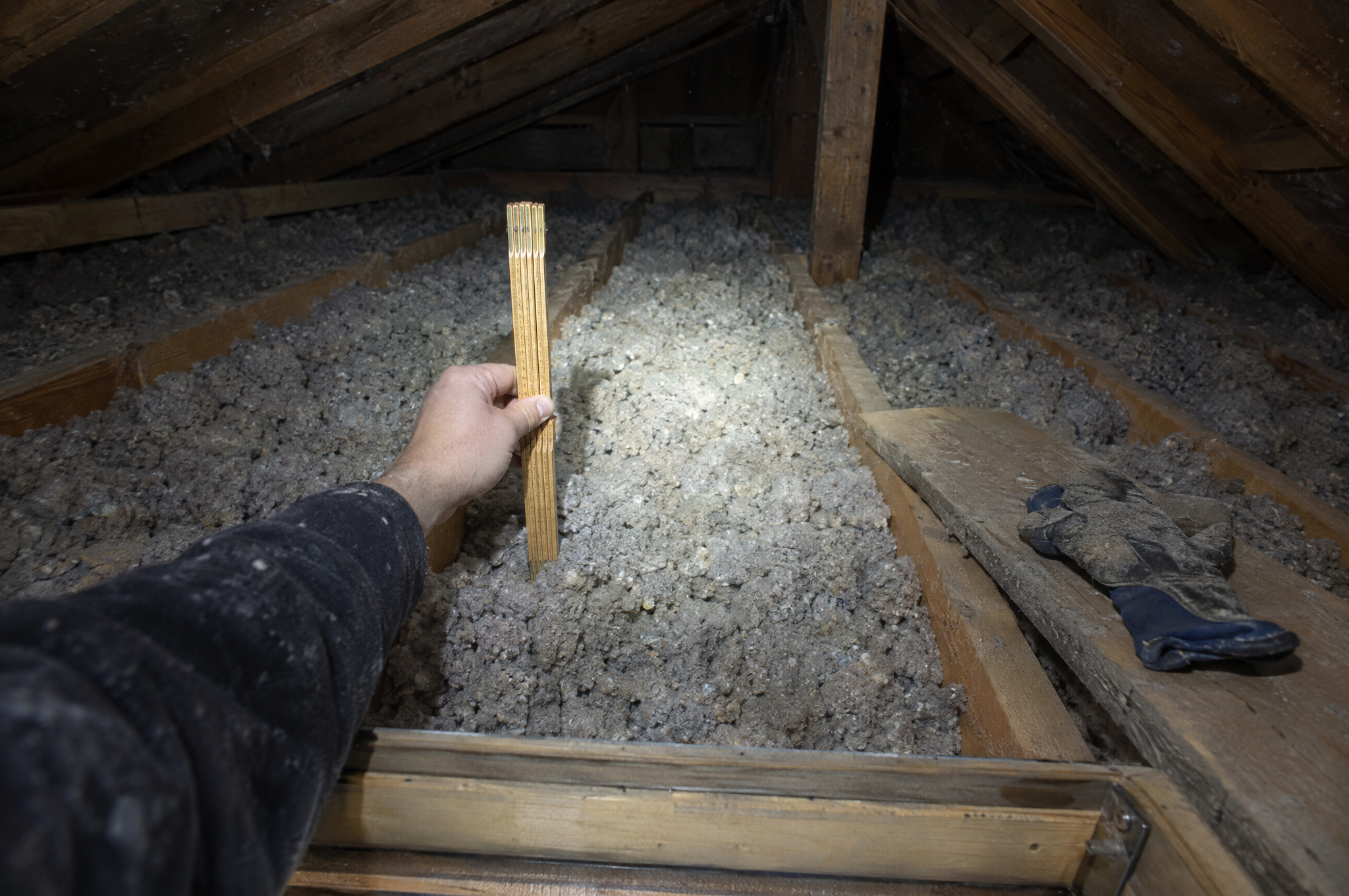 Folding ruler standing in attic loose-fill insulation between floor joists, lit by a headlamp